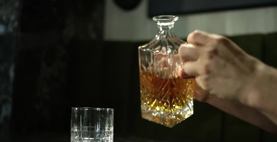 A man pours whiskey into a glass sitting on a black table