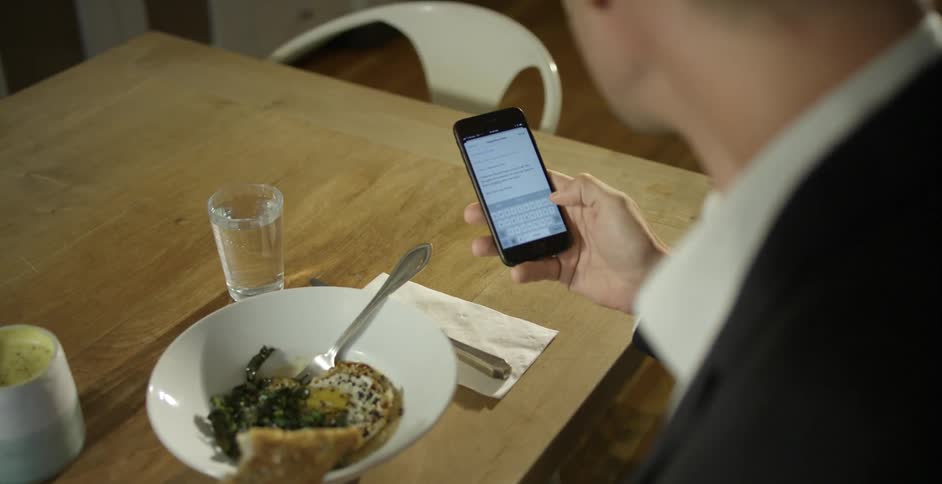 A man uses his smartphone while eating breakfast at a dining table