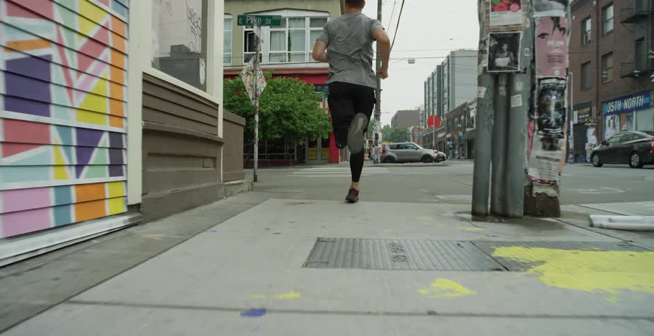 A man runs on the sidewalk of a large city and crosses an intersection