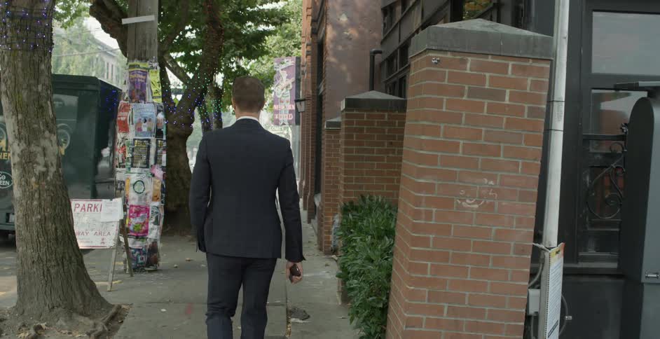 Man wearing a black suit and sunglasses holds a smartphone and walks down the street
