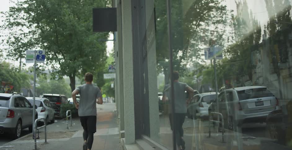 Man jogs along sidewalk passing row of parked cars