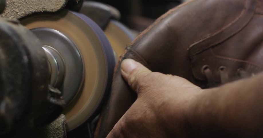A cobbler sanding the bottom of a boot