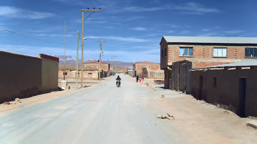 Pedestrians walk down the village road as a motorcycle rides by