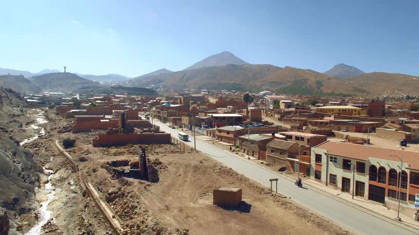 Motorcycle enters town paralleling dried river bed and mountains