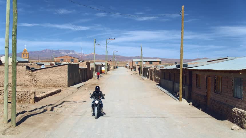 A person driving a motorcycle in a rural area as another person walks down the dirt road