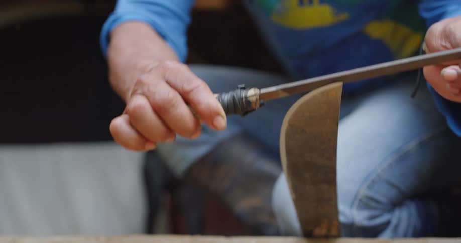 A person uses a metal file to sharpen a machete