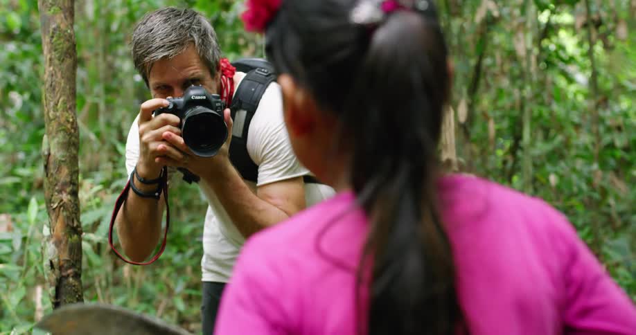 A man with a backpack and a camera taking a picture of a girl in the forest
