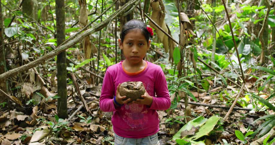 A child is holding a piece of fruit by the forest