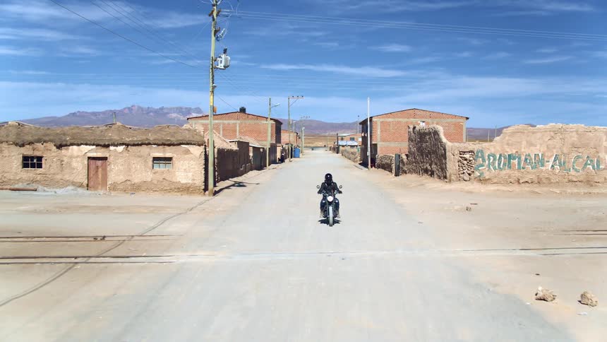 A motorcycle drives on an empty street through a dilapidated small rural town