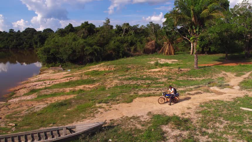 A man rides his dirt bike over to a boat by the lake