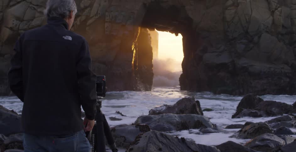 A man takes photos as waves crash between rocks