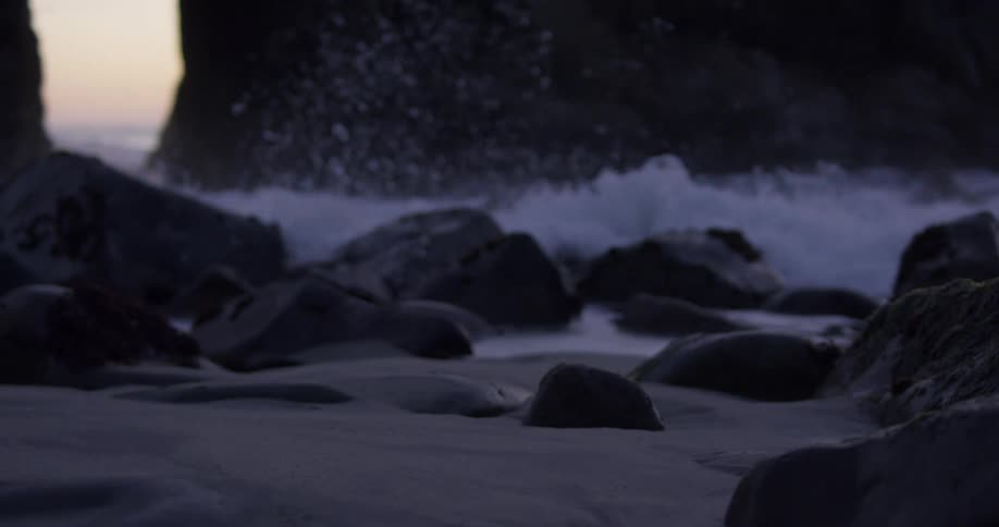Ocean waves washing over the stones and sand of a rocky beach during the day