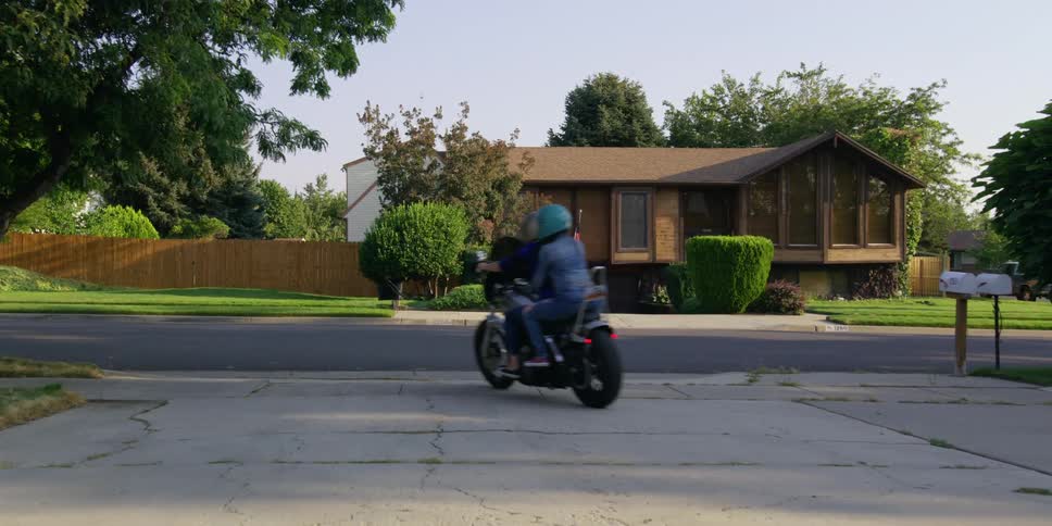 A motorcycle with driver and passenger pull out of a driveway to ride behind a fellow biker