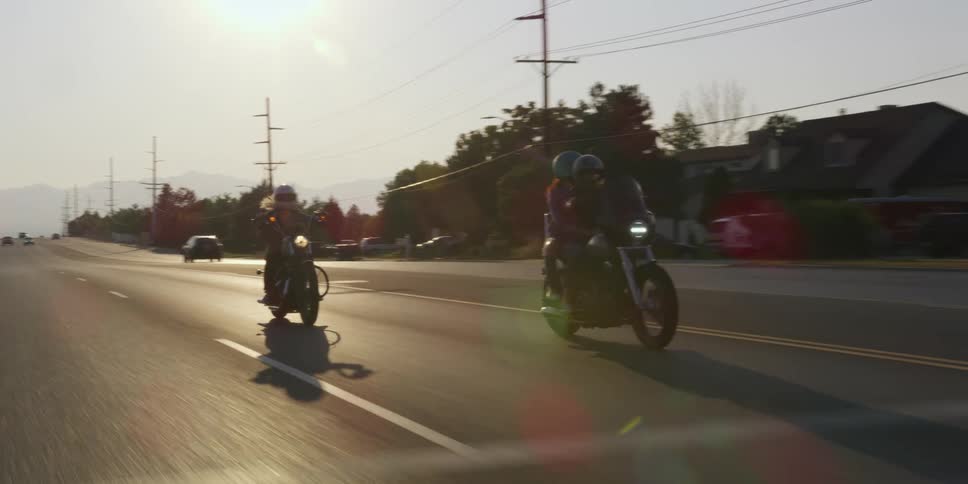 Three people with helmets on with two motorcycles on the road with trees and the sky in the background