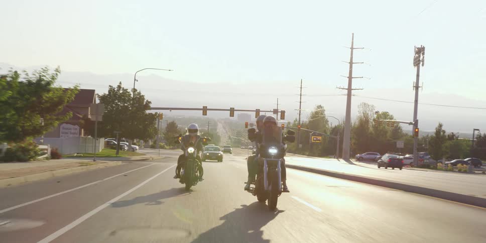 Two motorcycles riding on the street of a small town at day
