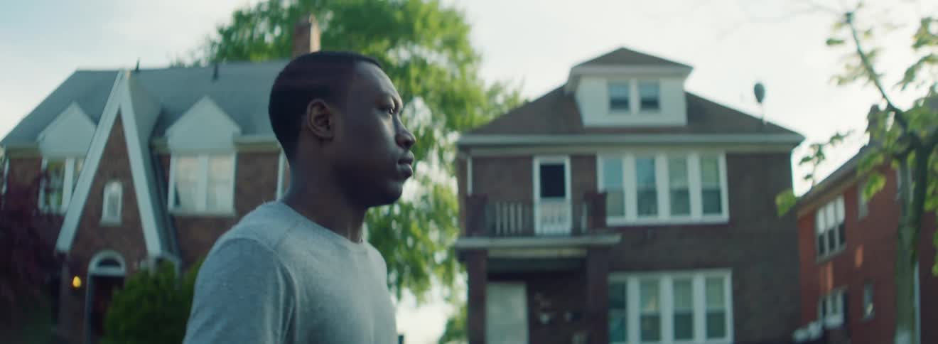 A man carrying a basketball walks out into a neighborhood street and starts to dribble as he walks