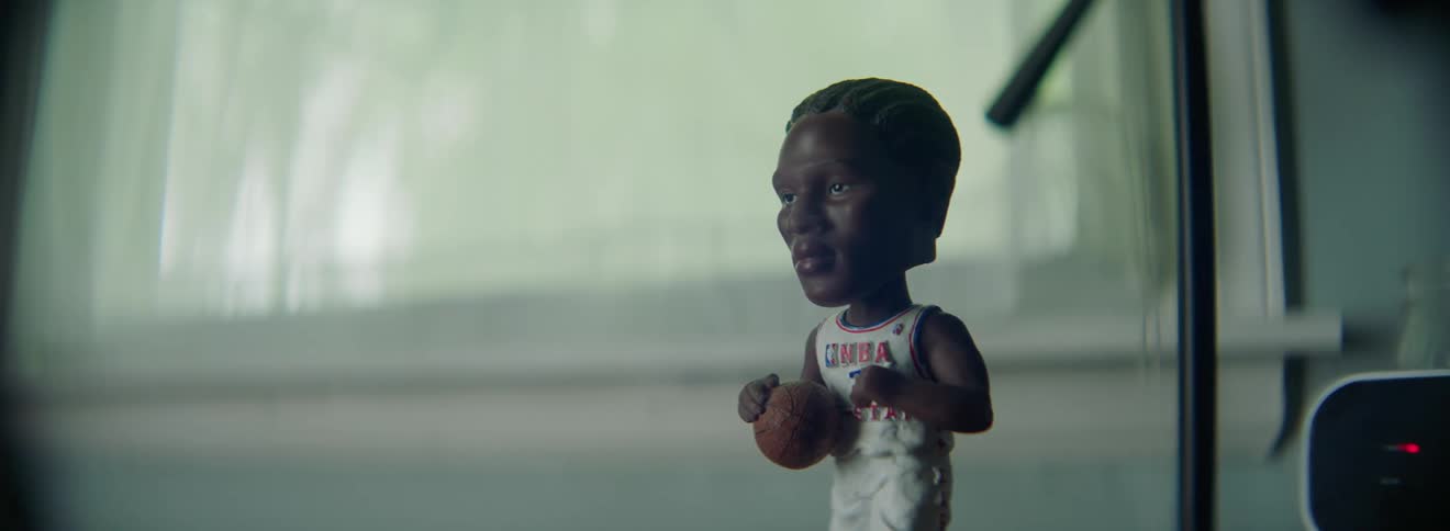 A bobblehead doll of an nba player with a window and a curtain in the background
