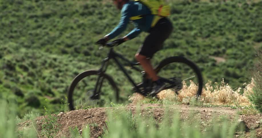 A male cyclist with cycling jersey and yellow bag cycles down a hill on a sunny day