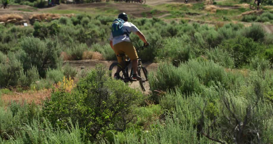 A man rides an electric bicycle along a dirt bike path through a hilly grassland