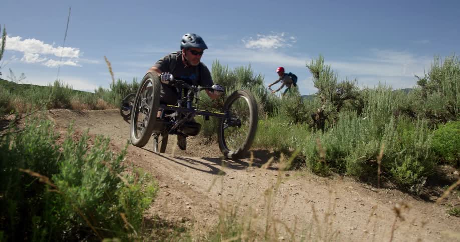 Cyclists ride their bikes on a dirt trail under a blue sky