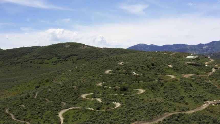 A group of cyclists ride down a dirt path on a large hill in the countryside