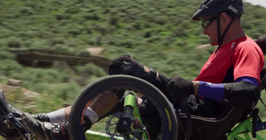 A man with a helmet and shades on a sports wheelchair riding on a trail