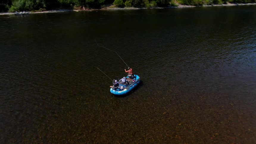 Three people sit in a raft in a large lake throwing a fishing line out to the water