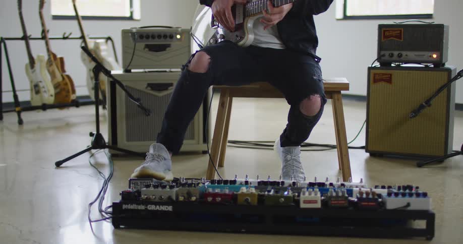 A man sitting on a bench playing a guitar with two windows behind him