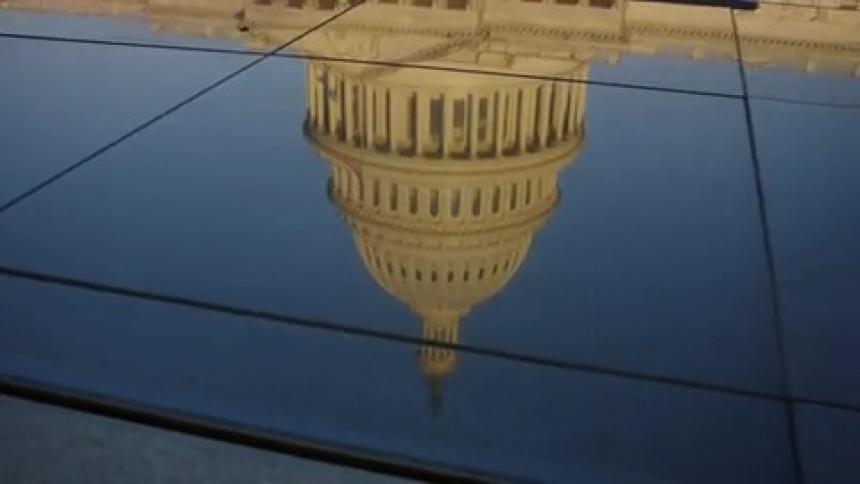 The white dome of the capitol building is reflected on panel surfaces on a bright blue sky day