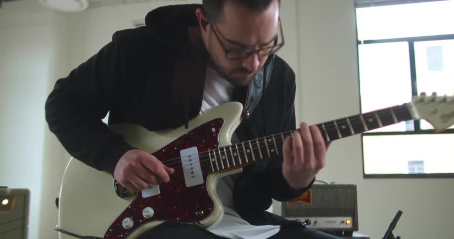 A man is sitting and playing an electric guitar