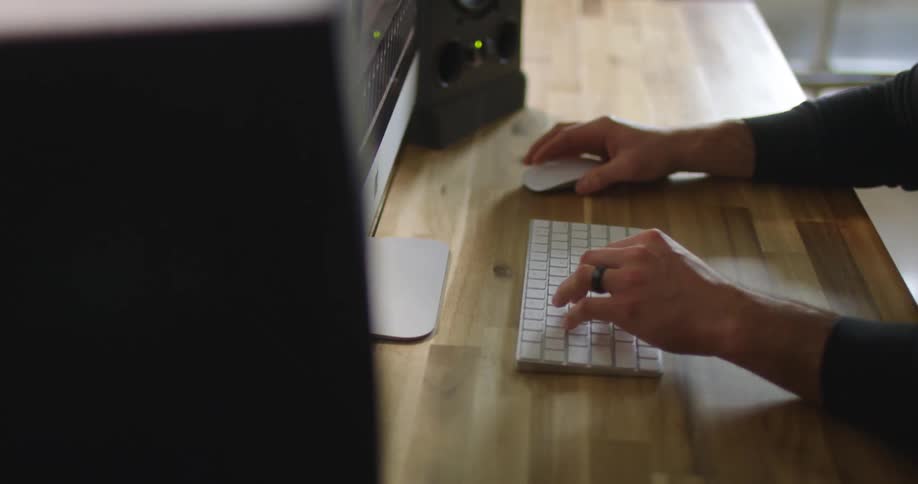 Man with a long sleeve black t shirt and a ring sitting at the desk uses a desktop in the office