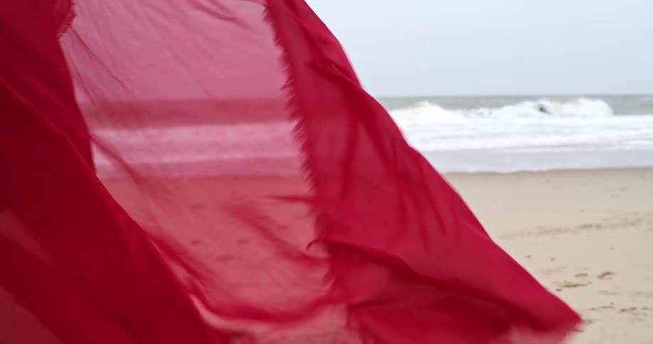 Wind blows through a red scarf on a sandy beach
