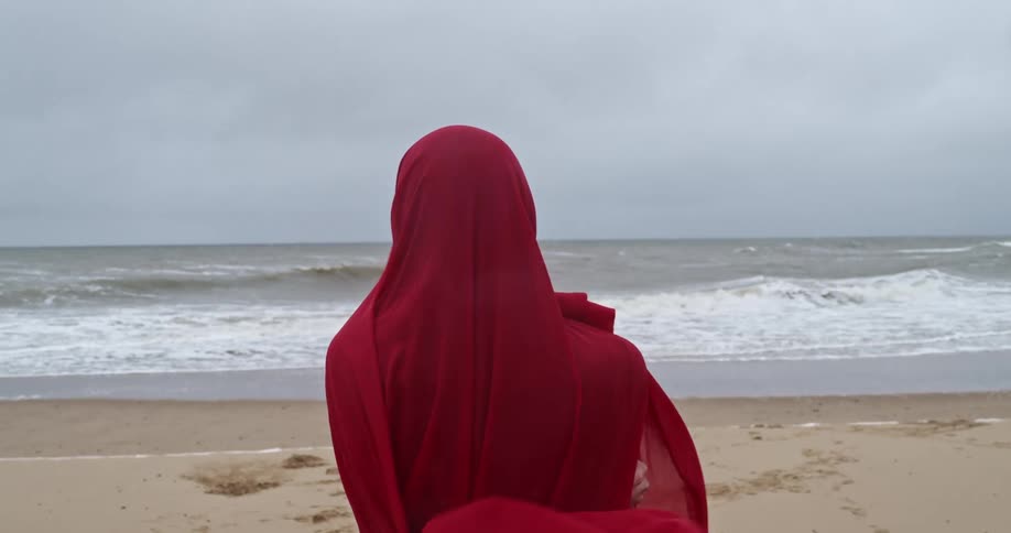 Wind blows through a womans red headscarf on sandy beach