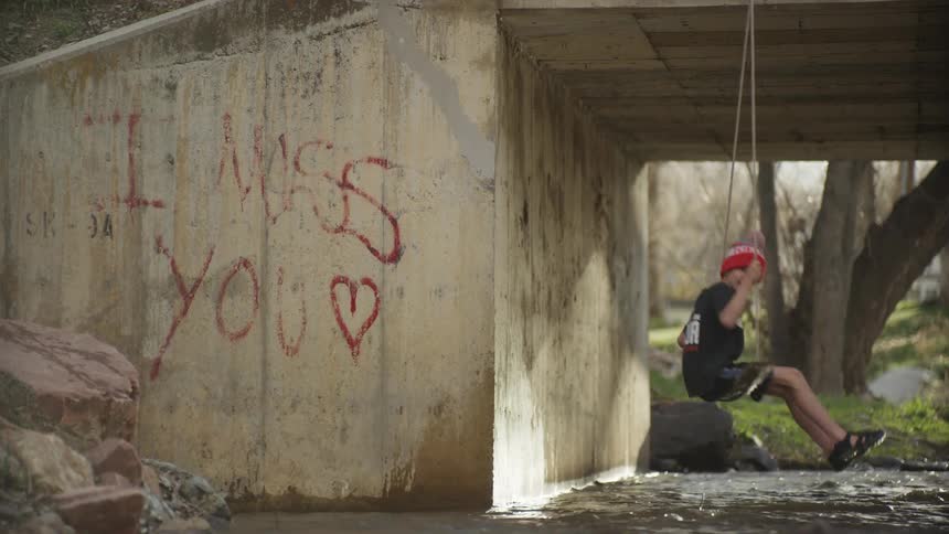 A child swings under a bridge with a small river flowing beneath him