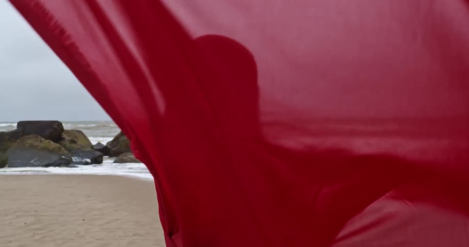 A woman covered up in a cloak walks towards the water