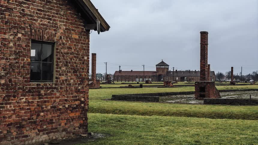 Buildings made with bricks with a grassy field and brick chimneys with the sky trees and clouds in the background
