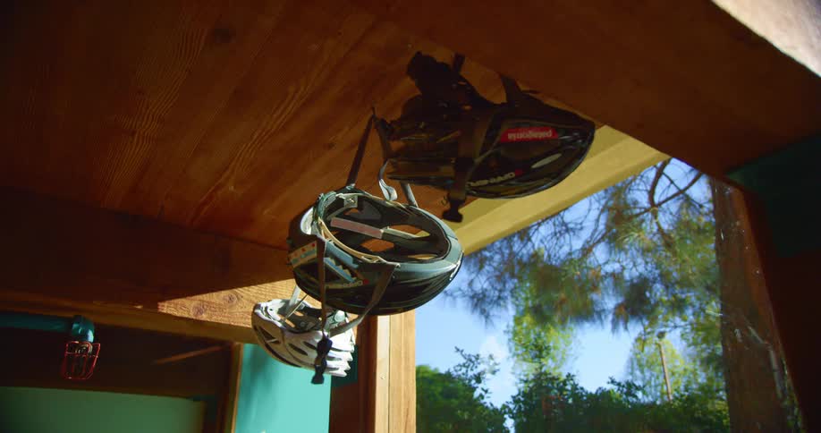 Bicycle helmets hand near wooden ceiling of porch opening onto pine tree