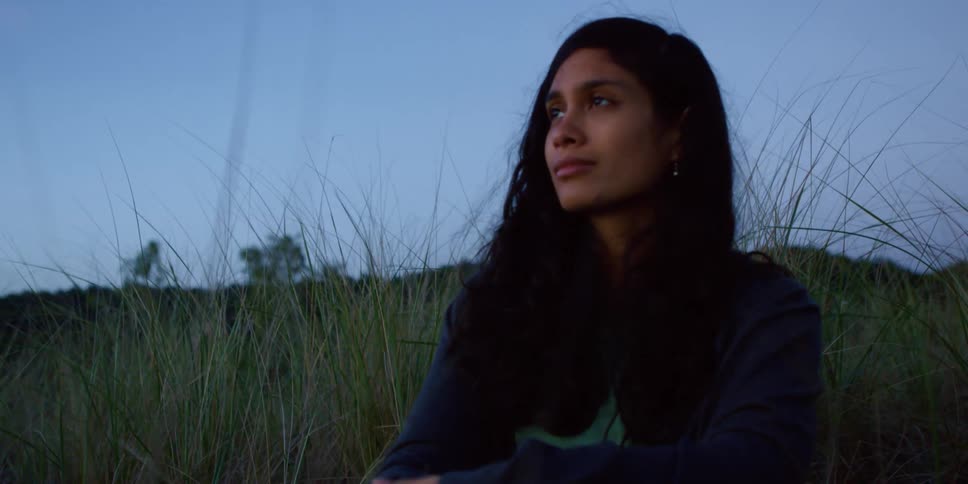 A woman is sitting outdoors in a grassland area