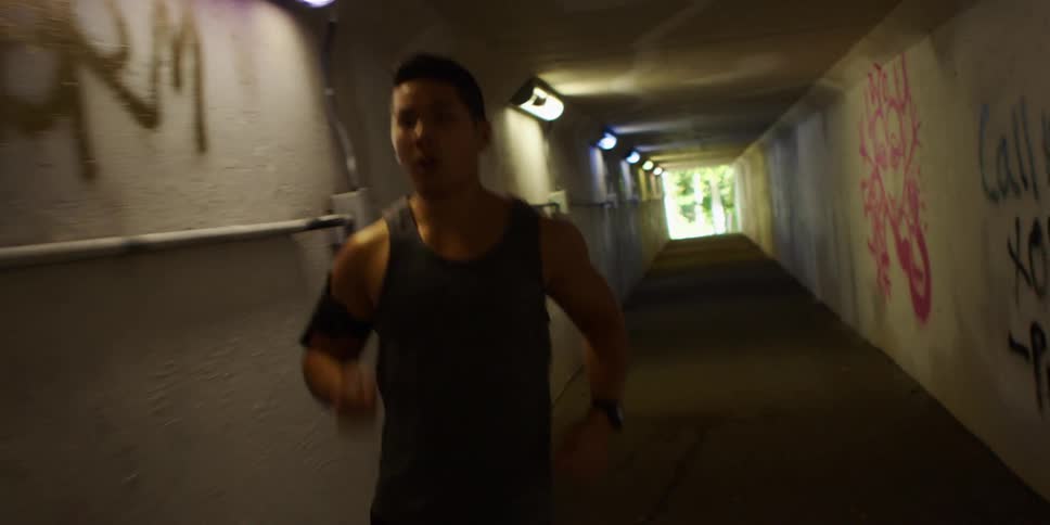 Man covered in sweat jogs through a tunnel with a smartphone on an armband