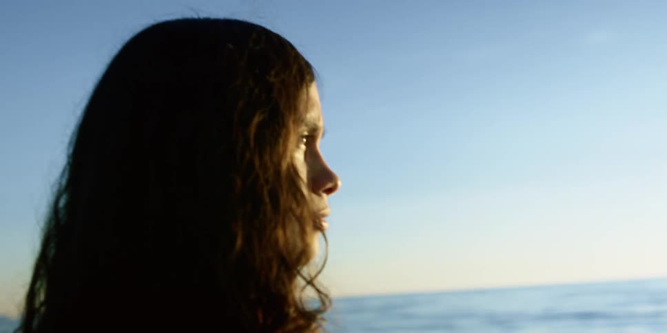 Curly hair brunette girl watches sea at sunset