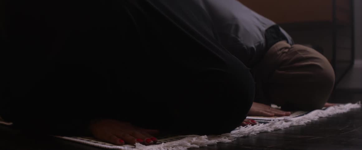 Two women kneeling on rugs lean forward on the floor to pray