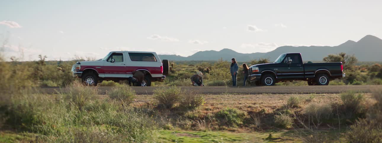 A young girl brings a man a tool as they are both stopped on the side of the road