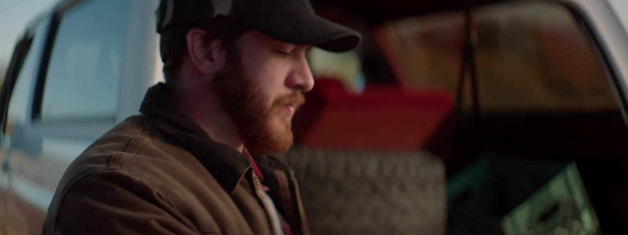 Bearded man wearing baseball cap exits a car on the road and pays someone with dollar bills