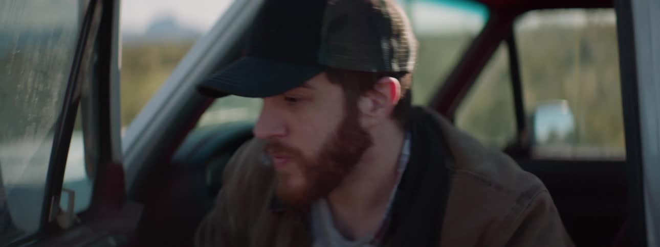 A man gets out of a parked car and inspects the front of the vehicle