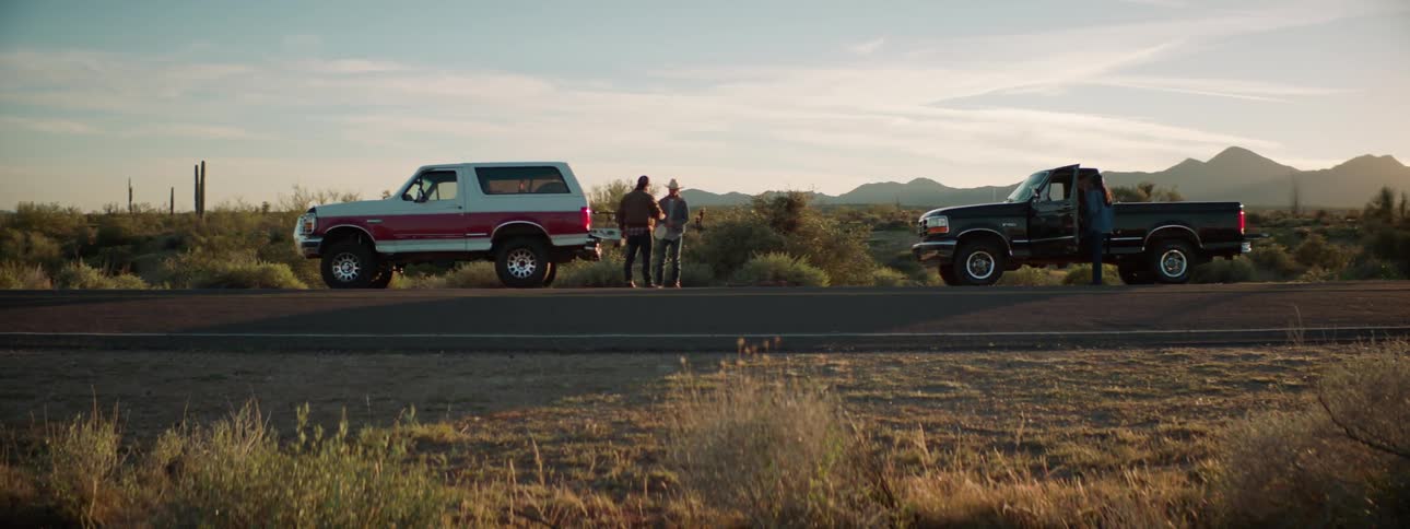 Two people stand in between vehicles sitting along side a country road
