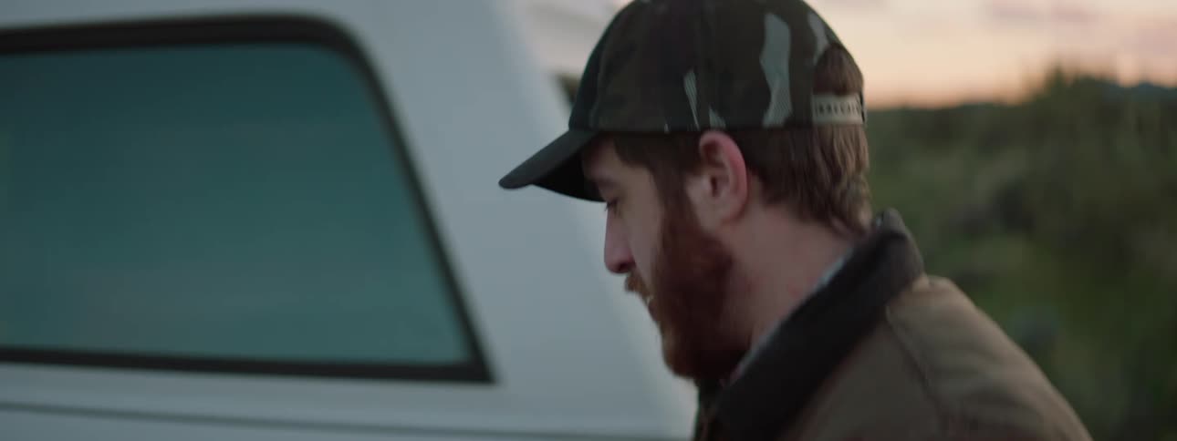A smiling man in a hat enjoys a sunset and walks to his truck