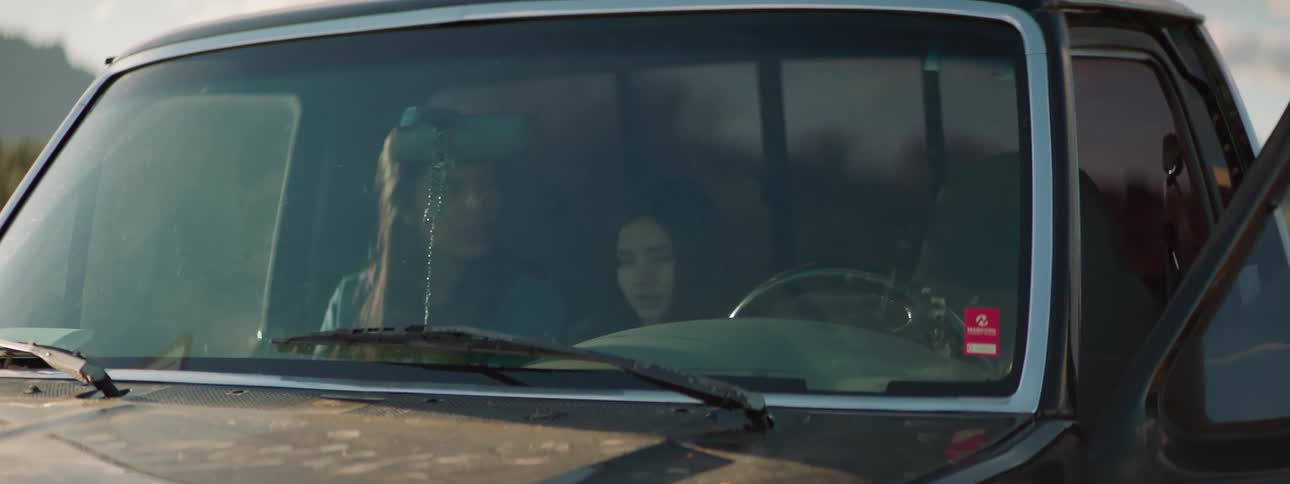 A teenager and child sit in a truck with a man who opens the door and gets out