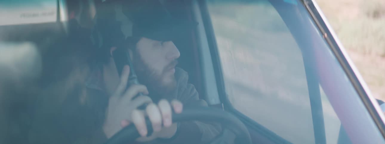 A man drives in a vehicle while talking on a phone