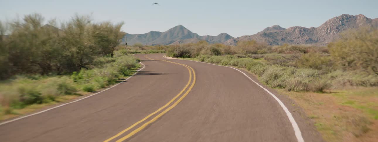 Empty road winds through scrub land toward mountains