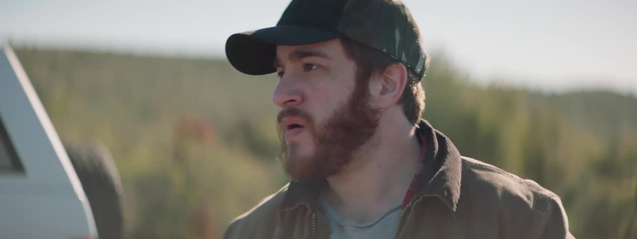 Man with beard and a cap looks around and gets in a car in the middle of the road